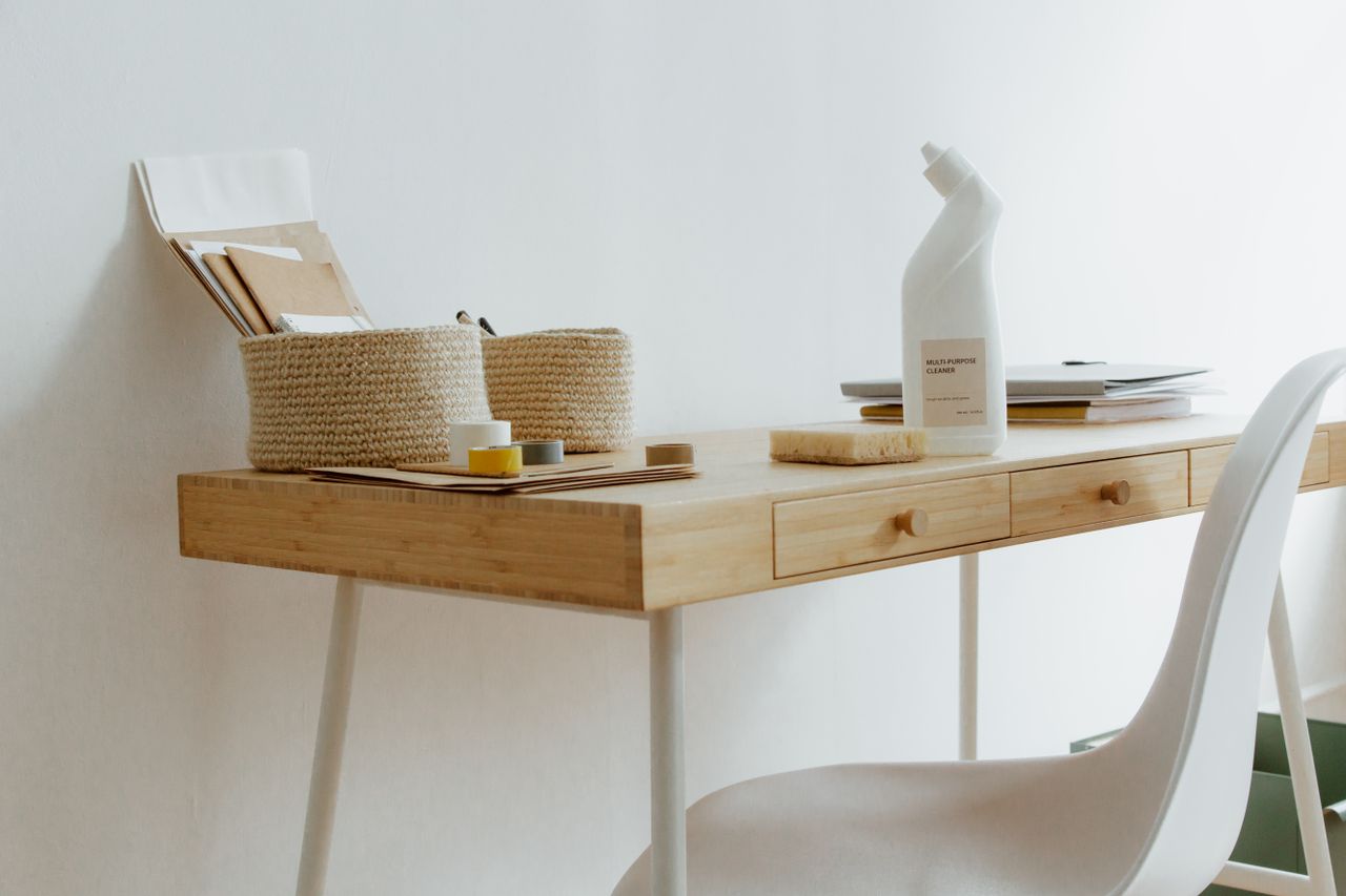 Un bureau à domicile propre et bien rangé avec des produits de nettoyage, des papiers et des paniers de rangement.